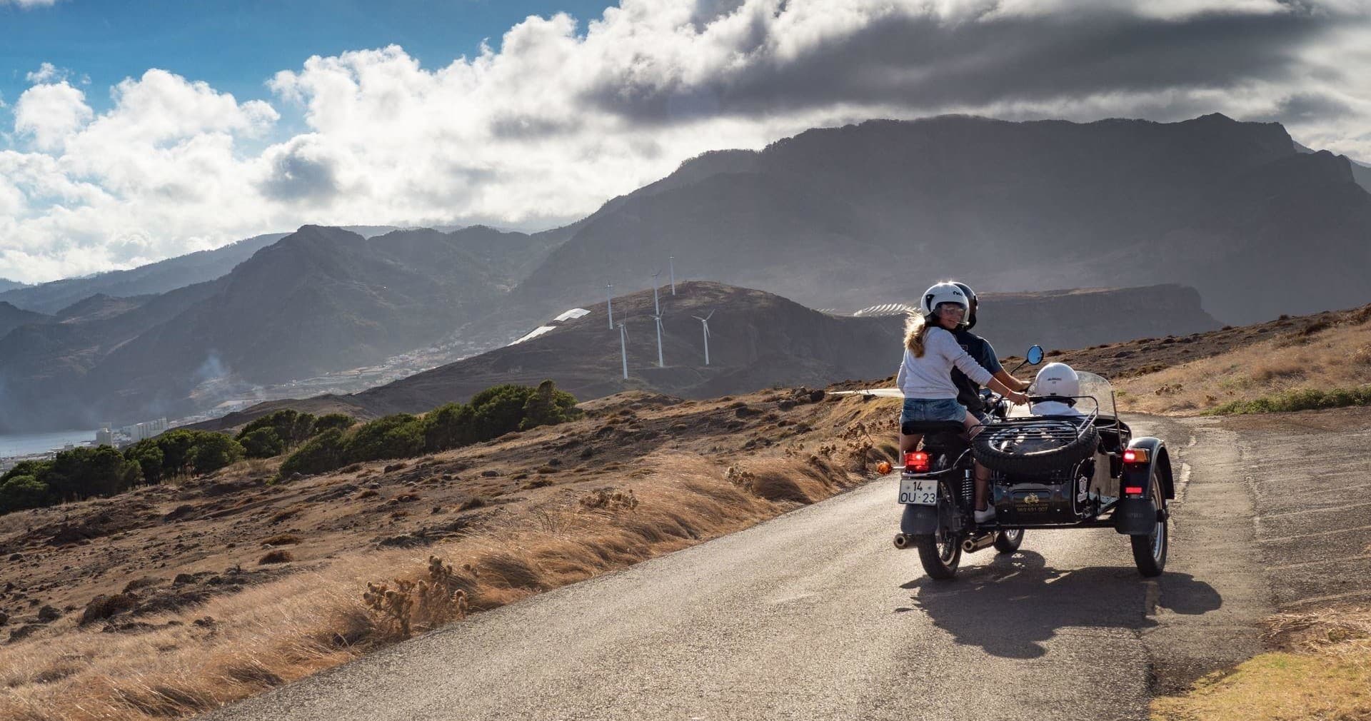 Sidecar motorcycle on rugged coastal road with mountain backdrop
