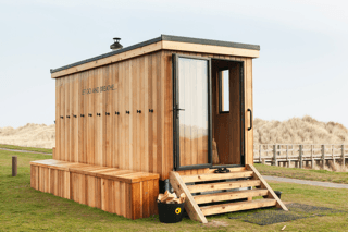 Mobile wooden sauna hut on windswept dunes overlooking sea