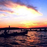 Sunset silhouette of kayaks on calm lake, dramatic coastal sky