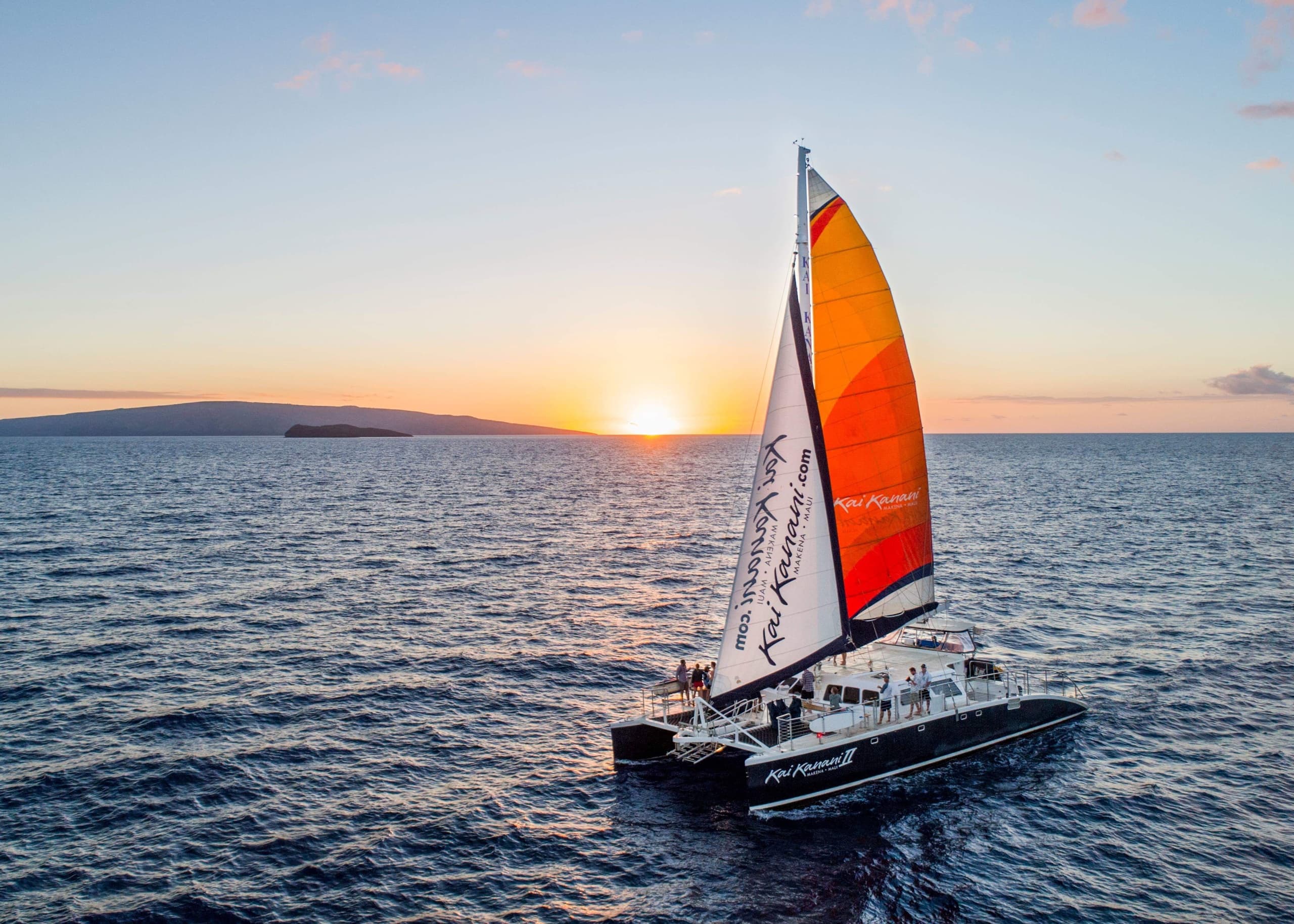 Sailboat with orange spinnaker sailing at ocean sunset