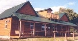 Large rustic log cabin lodge with porch in green countryside
