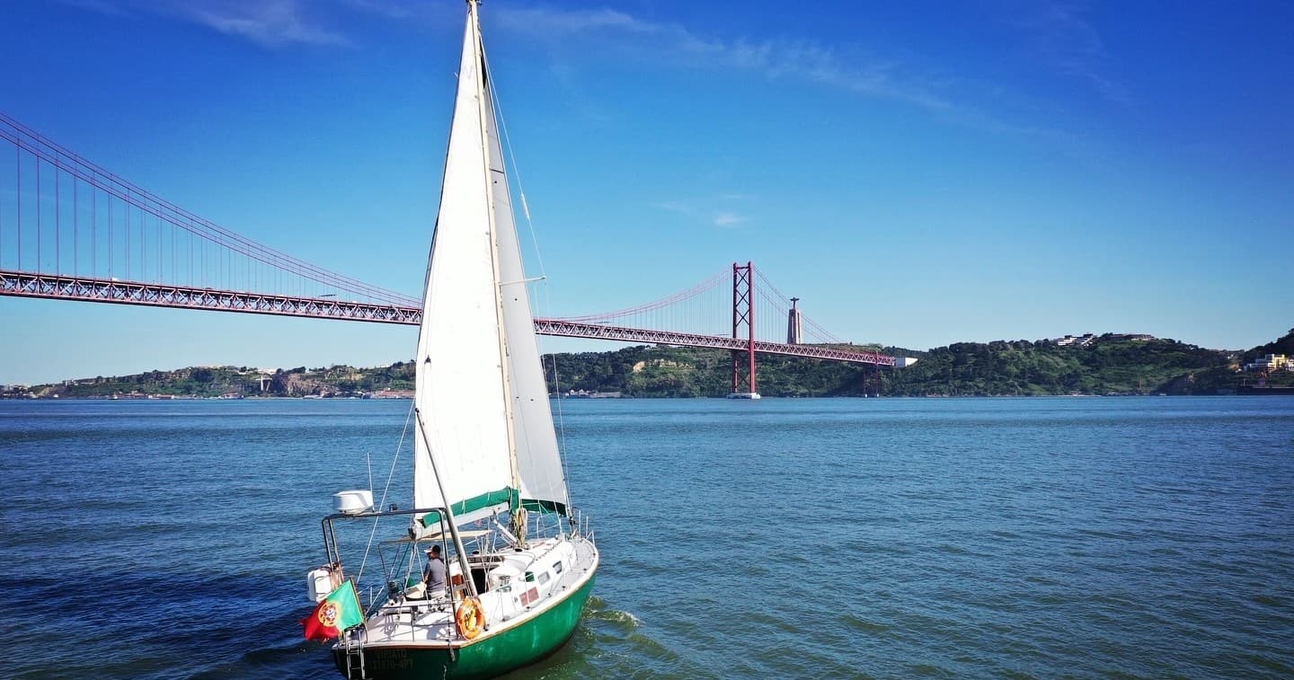 Sailboat cruising near 25 de Abril Bridge on Tagus River