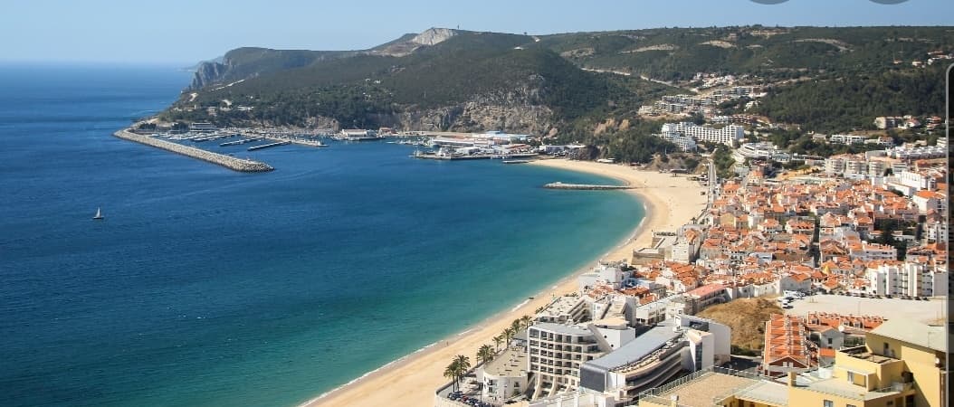 Sweeping Nazaré bay aerial with broad surf beach, coastal scenery and waves