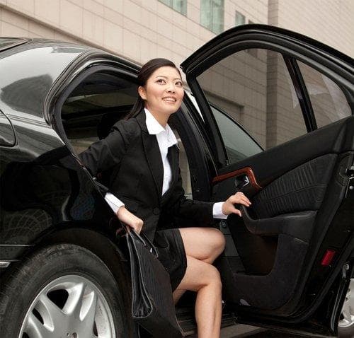 Businesswoman stepping from black sedan onto city sidewalk with bag