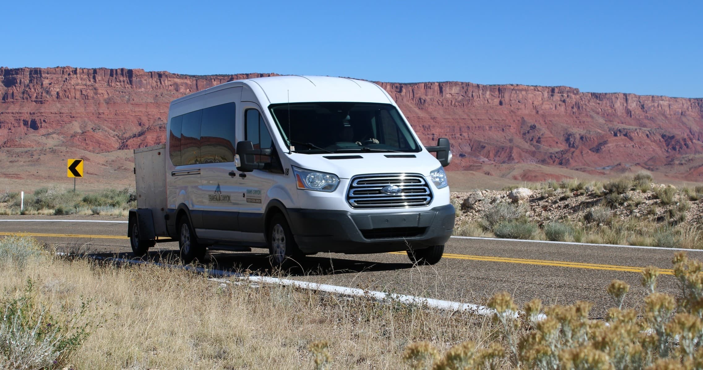 Shuttle van towing gear along desert highway near canyon