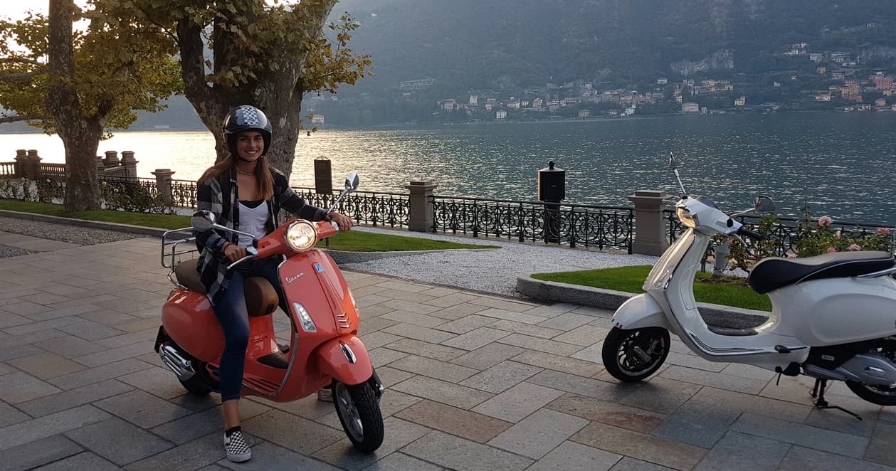 Person posing on red scooter on lakeside promenade at Lake Como