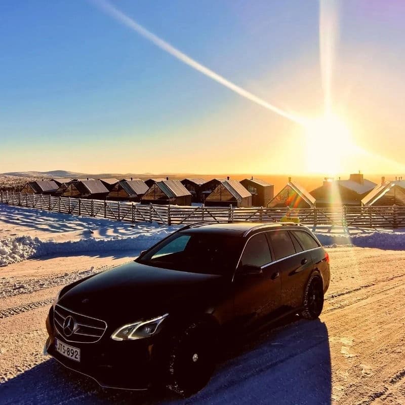Sunrise over snowy road with tour car parked on Arctic coastline
