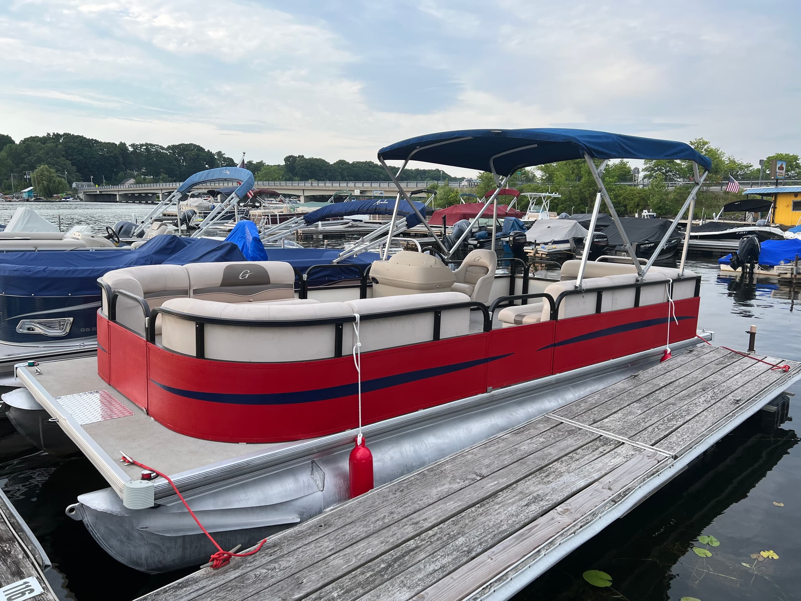 Red pontoon boat tied at busy marina dock with other boats