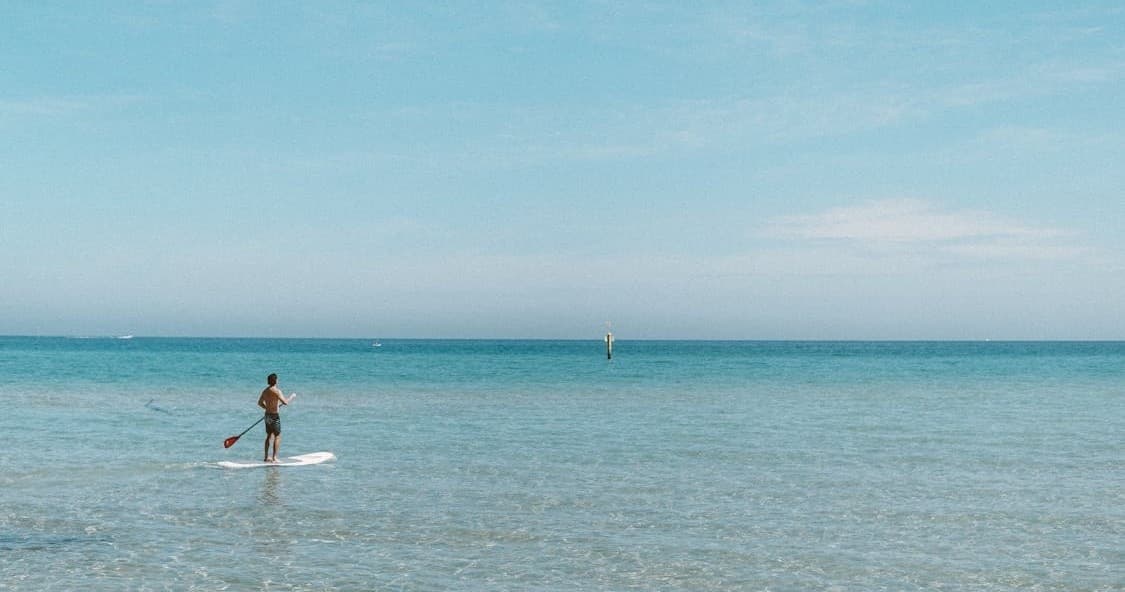 Stand-up paddleboarder on calm ocean with expansive horizon