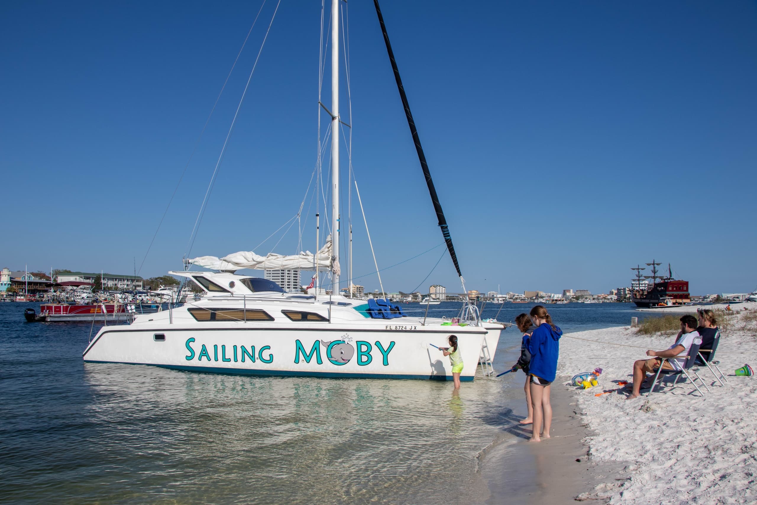 Sailing catamaran docked at sandy beach with passengers boarding