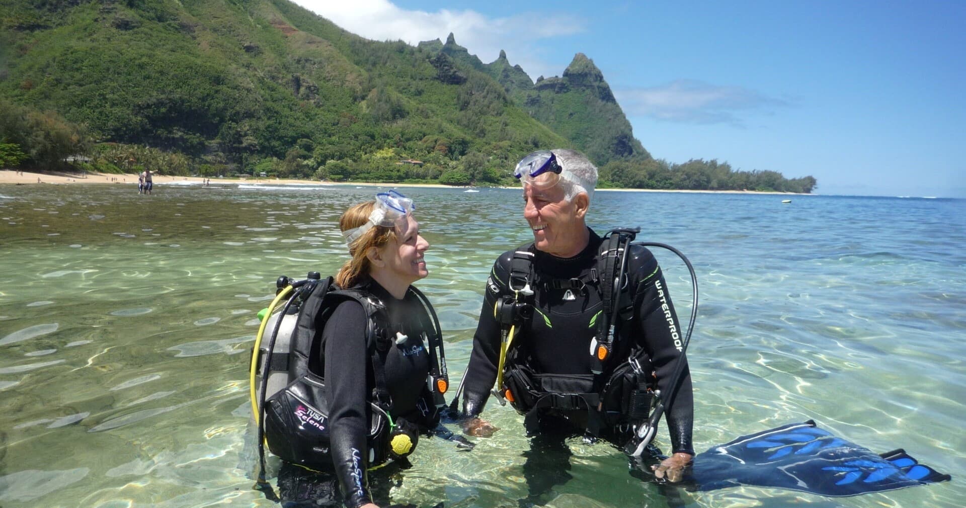Couple preparing for shore dive in tropical bay with volcanic peaks