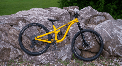 Yellow full-suspension mountain bike on rocky trail beside park