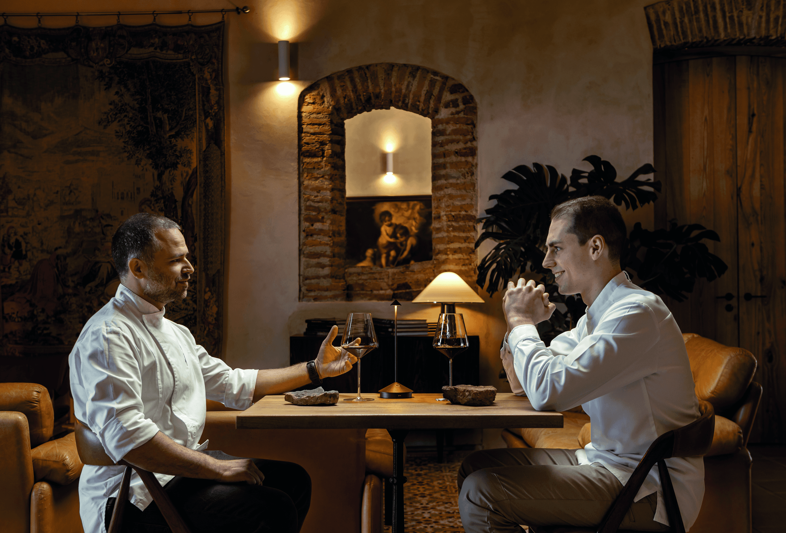 Two chefs conversing at intimate restaurant table during dinner
