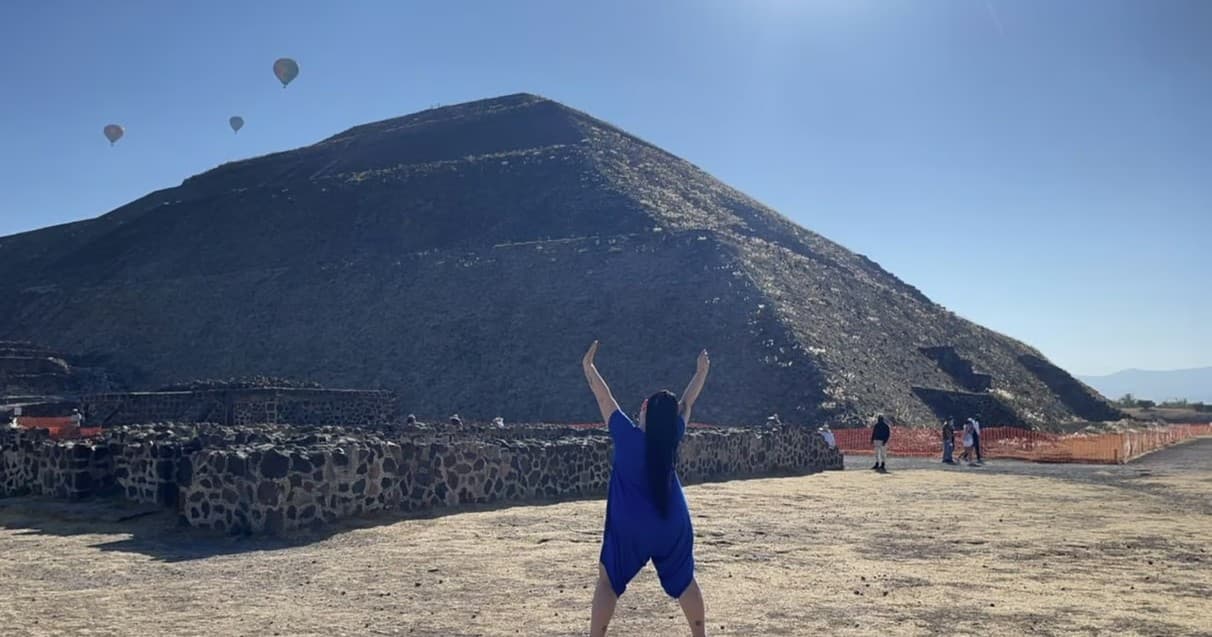 Person cheering at Teotihuacan pyramid with hot air balloons