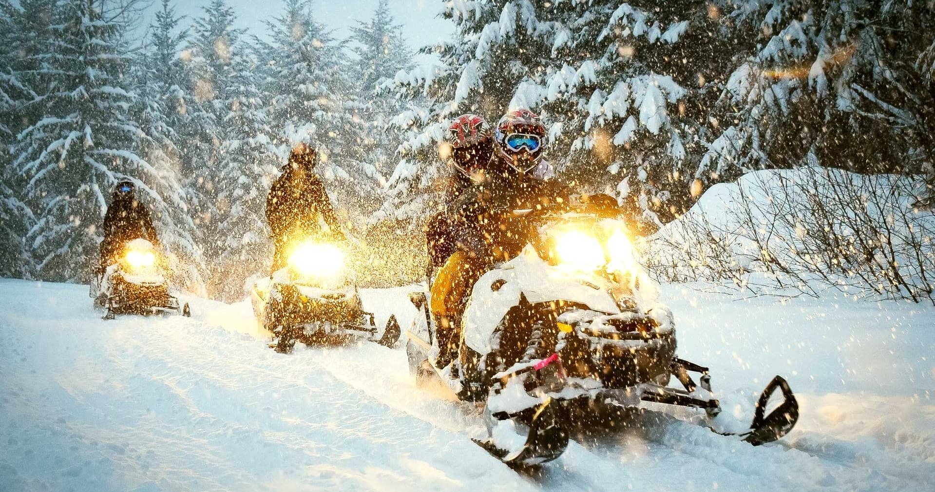 Snowmobilers riding through snowy forest trail in winter storm
