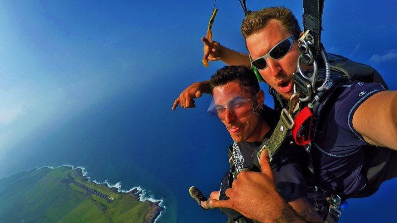 Tandem skydivers taking a selfie above ocean cliffs