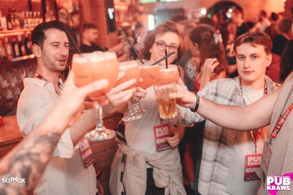 Friends toasting drinks at a crowded bar during pub crawl