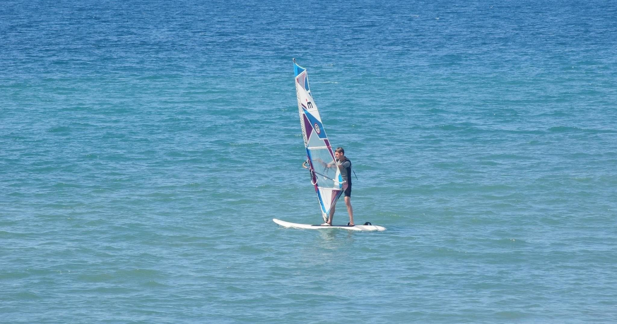 Solo windsurfer on calm turquoise sea near Gran Canaria shoreline