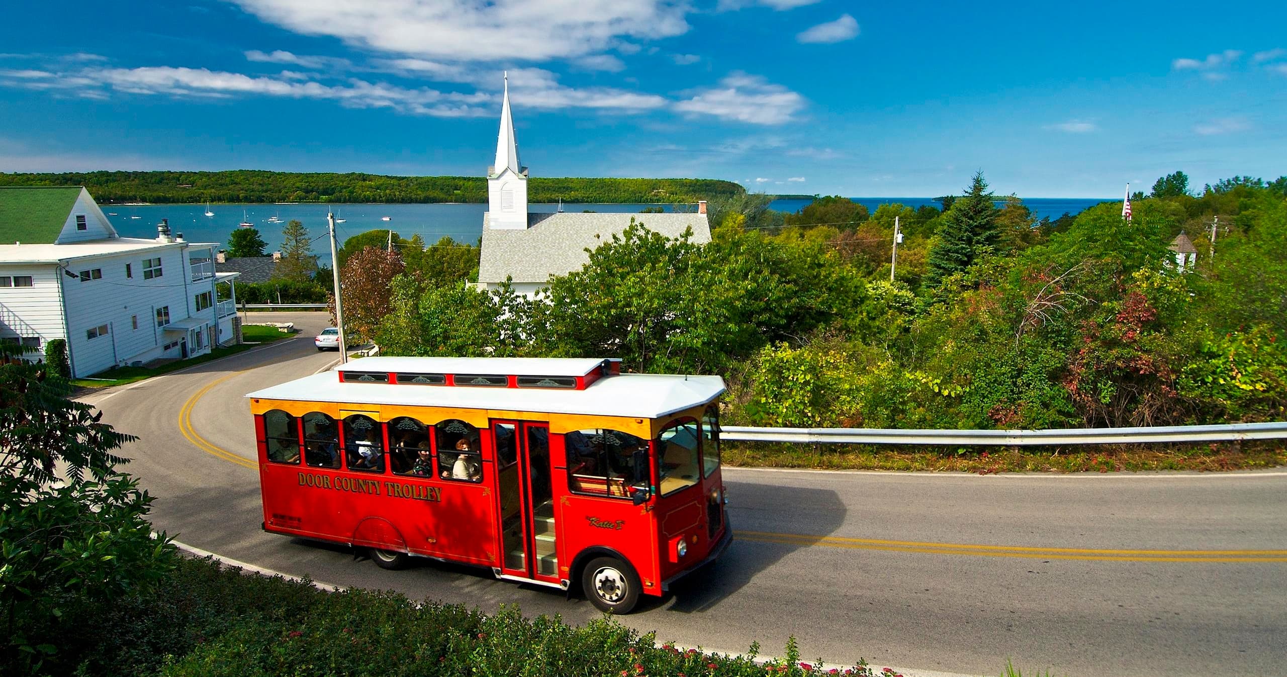 Red trolley driving past church along Door County shoreline