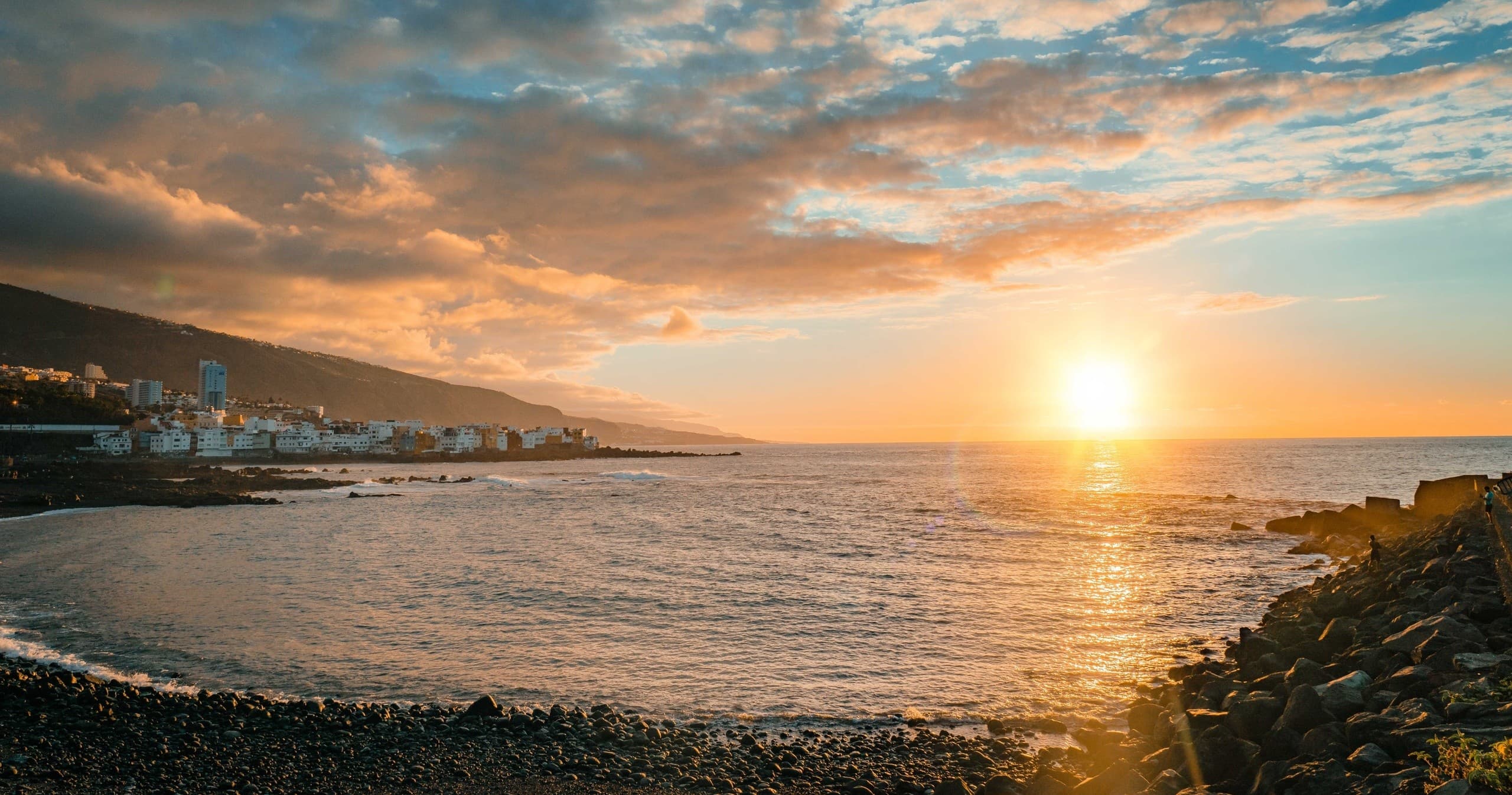 Sunset over rocky coastal bay with distant town skyline