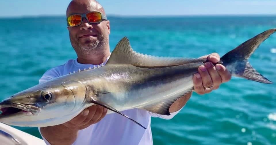 Fisherman displaying large wahoo fish over turquoise sea on boat