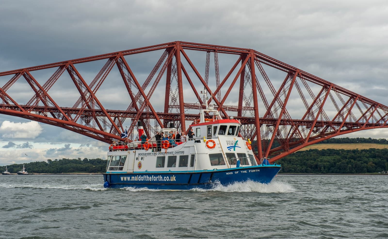 Sightseeing boat passing under the Forth Bridge near Edinburgh