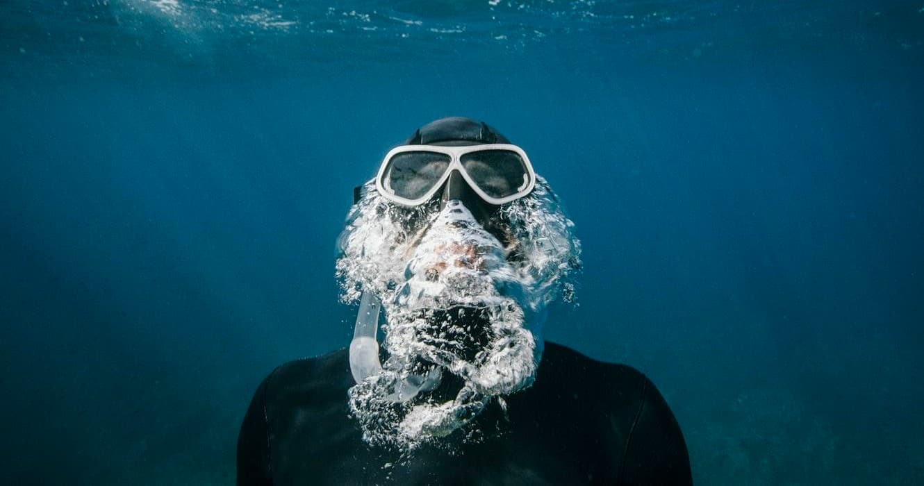 Scuba diver exhaling bubbles underwater with goggles in ocean