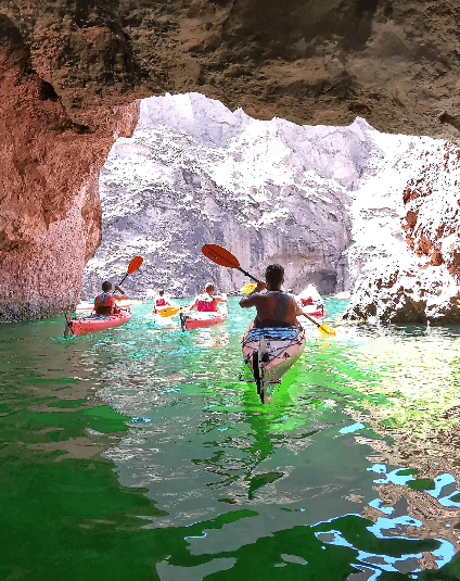 Group kayaking through cave entrance into sunlit canyon waters