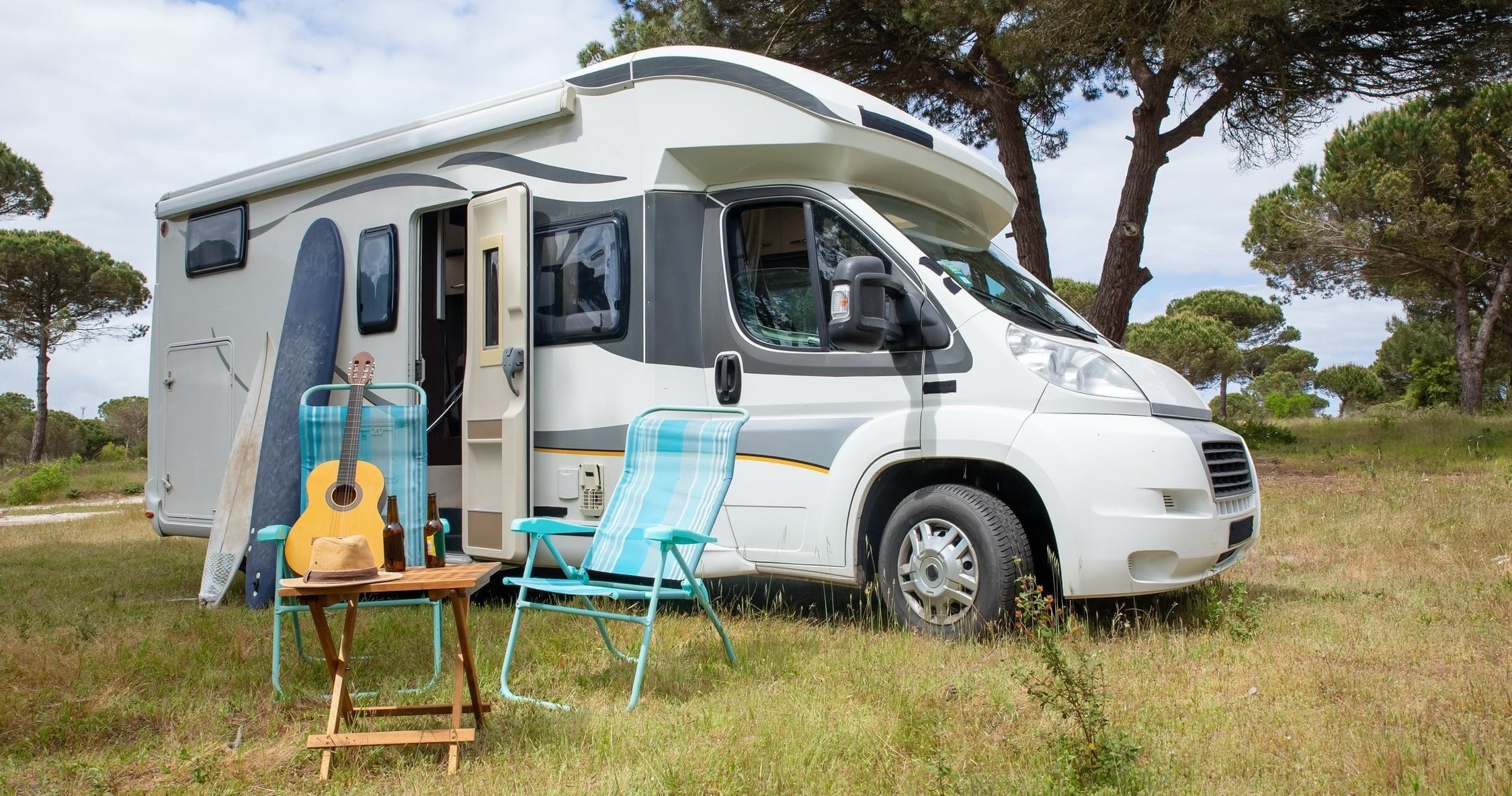 Campervan parked at grassy campsite with chairs and guitar