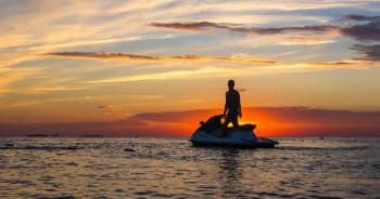 Jet skier silhouetted at sunset over calm coastal waters