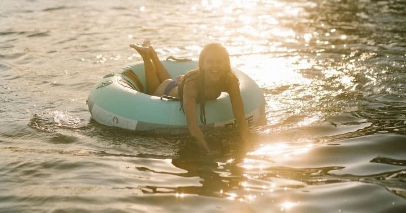 Person lounging on inflatable tube at golden sunset on lake shore