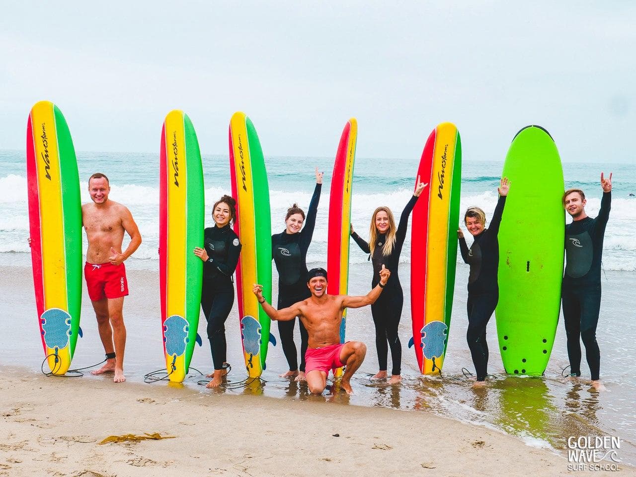 Group of surfers with colorful boards posing on sandy beach