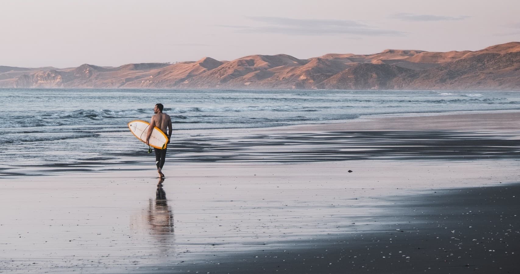 Surfer walking along wide sandy beach at low tide, coastal vista