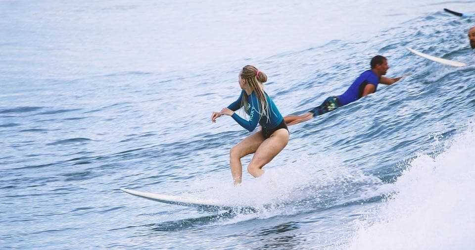 Two surfers paddling on longboards at calm ocean horizon, lesson scene