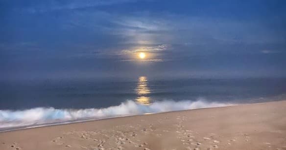 Moonrise over sandy beach with ocean reflection