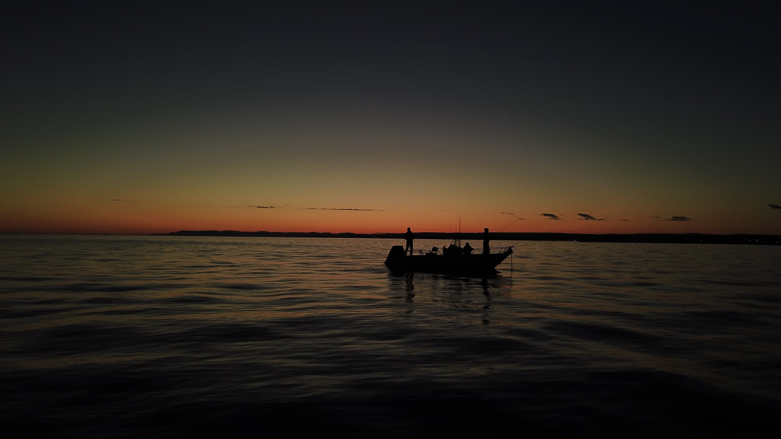 Silhouette of anglers in a boat at dramatic sunset on sea
