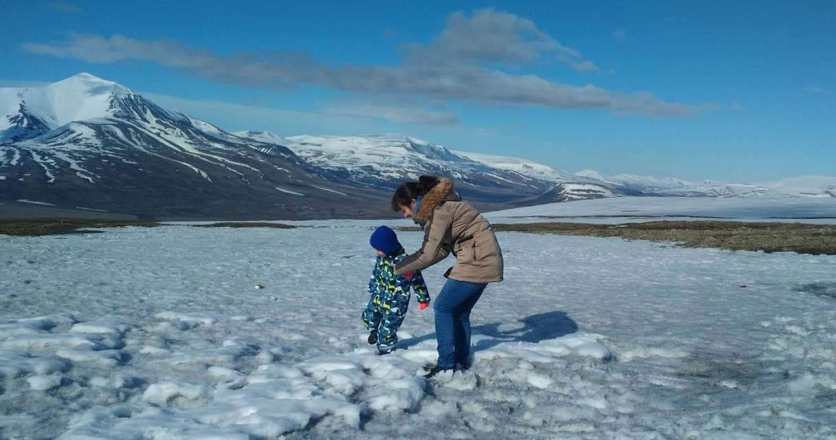 Parent and child exploring frozen shoreline with mountain views