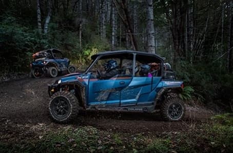 Blue UTV parked among dense woods on muddy off-road track