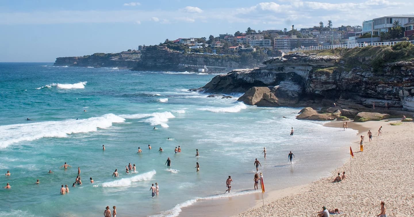 Sunny sandy beach with swimmers and ocean surf