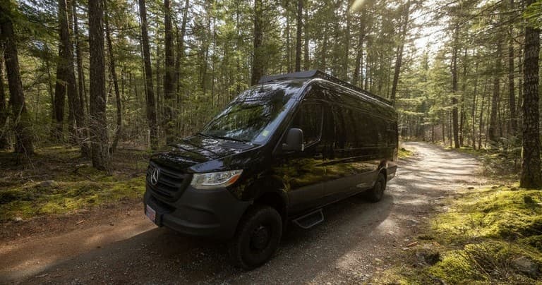 Black camper van parked on forest trail for van camping