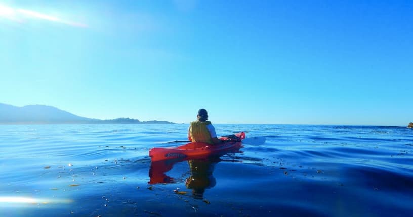 Solo kayaker paddling on calm open ocean under blue sky