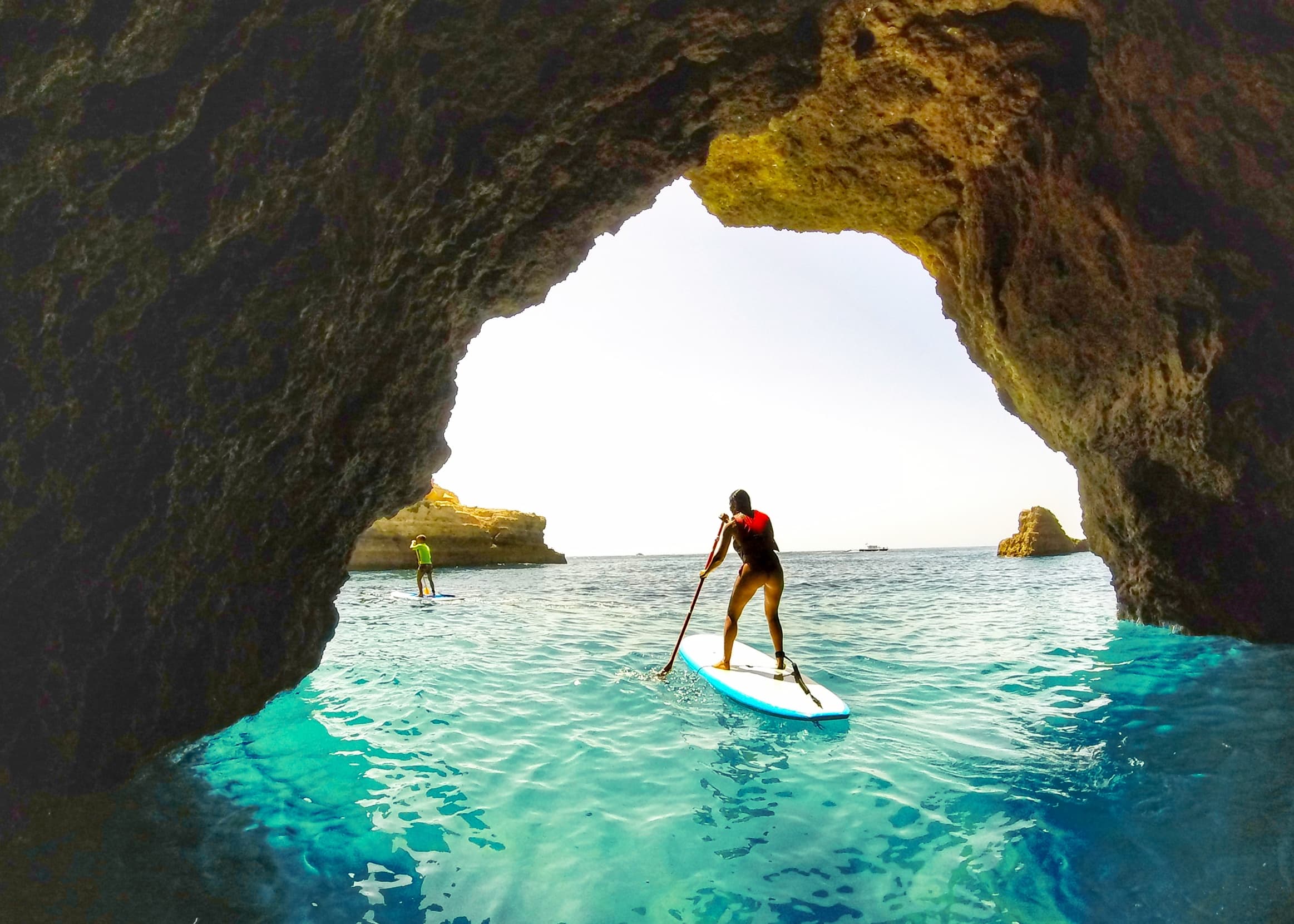 Paddleboarder exploring turquoise sea cave framed by cliffs