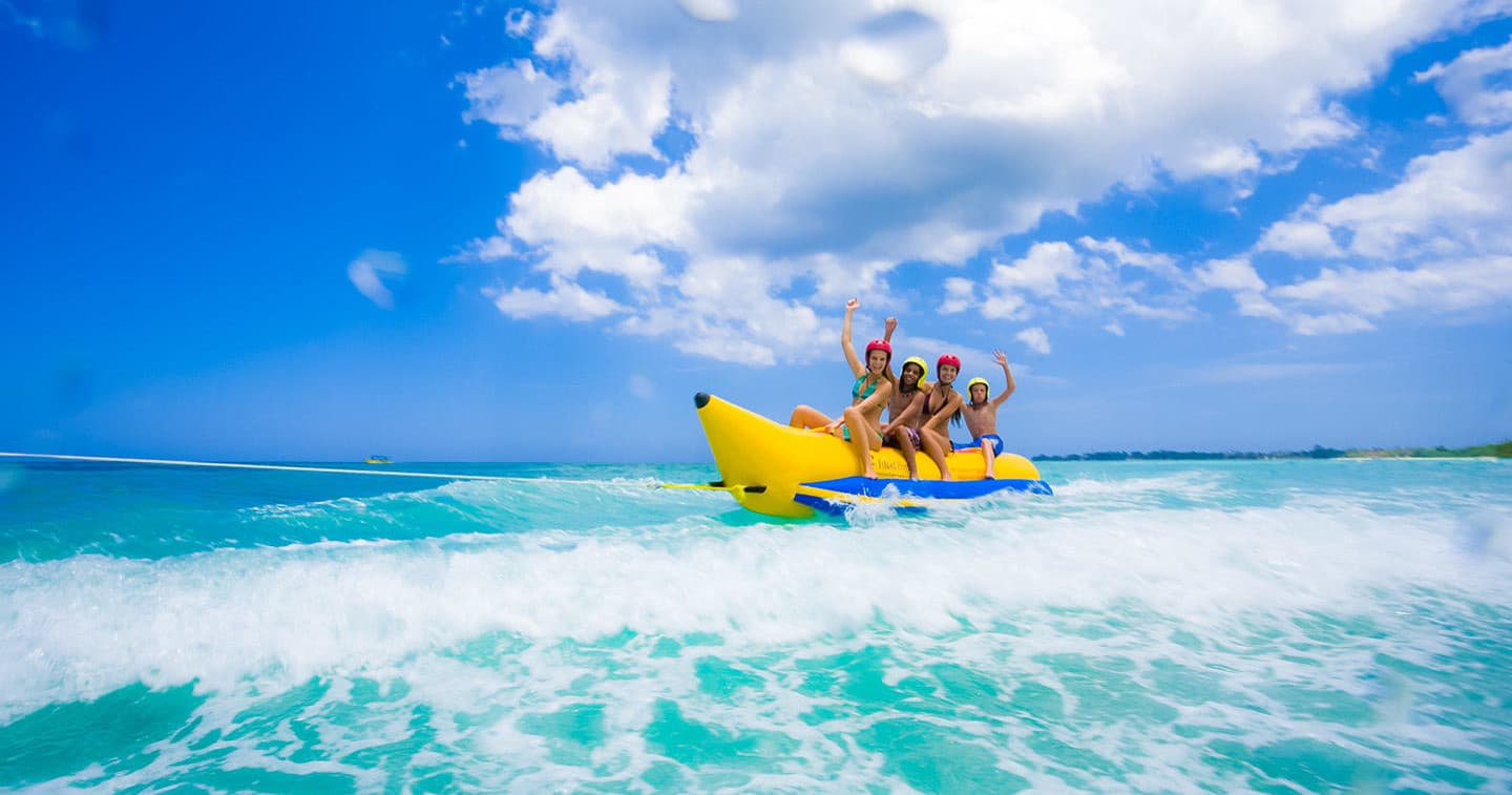 Group riding banana boat across turquoise ocean under blue sky