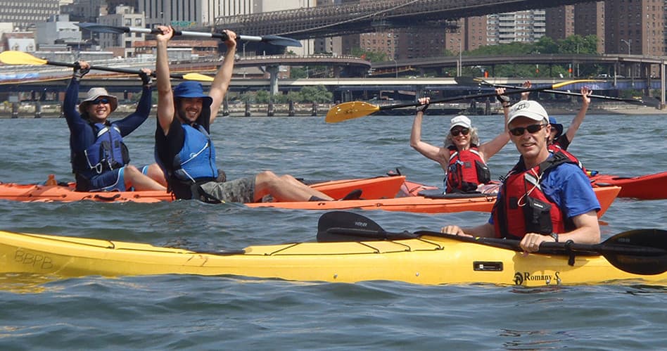 Smiling kayakers waving from bright kayaks on city river
