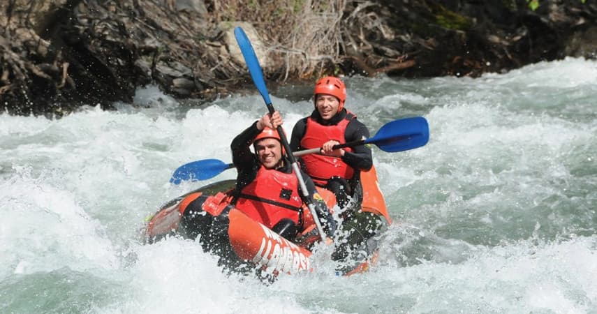 Two kayakers paddling inflatable kayak through frothy whitewater rapids