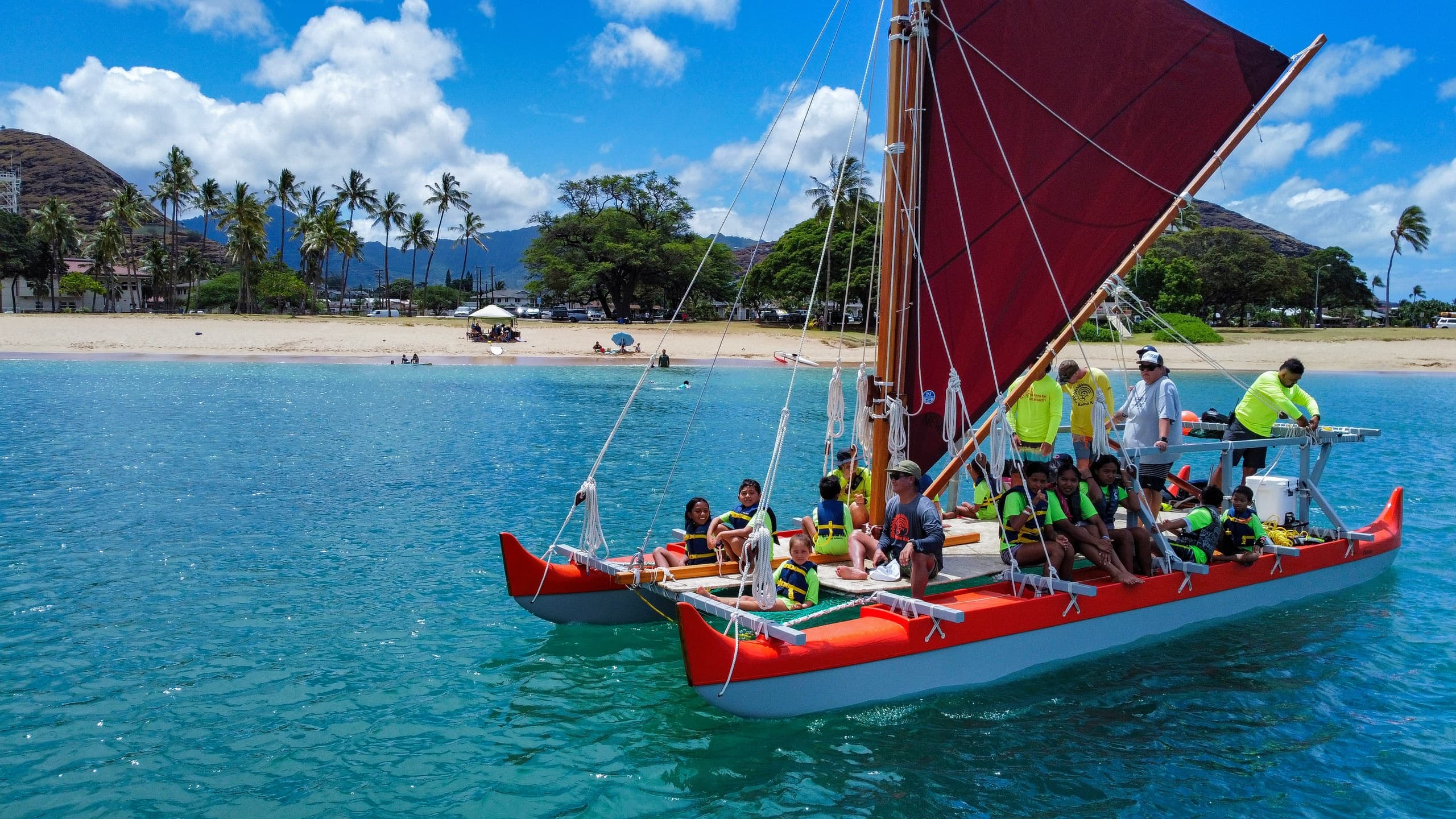 Traditional Hawaiian voyaging canoe with sail off tropical beach