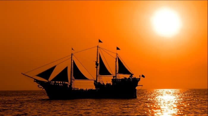 Silhouette of tall sailing ship at sunset over calm ocean