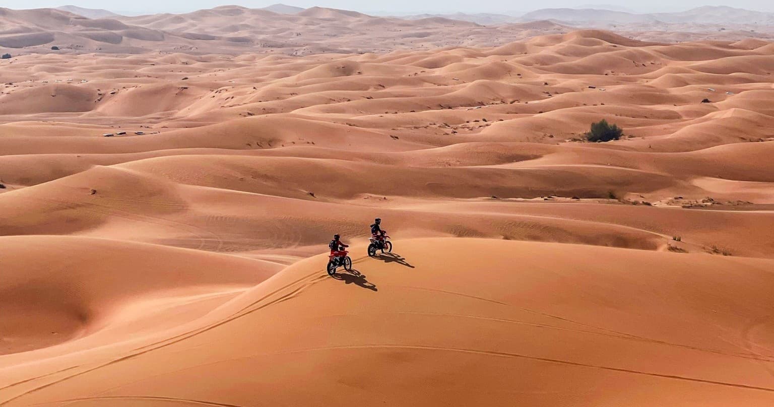 Two riders traversing sandy desert with cones and dust
