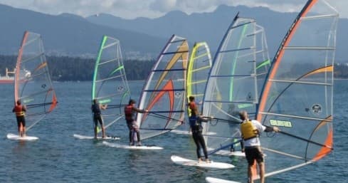 Multiple windsurfers with colorful sails on coastal water