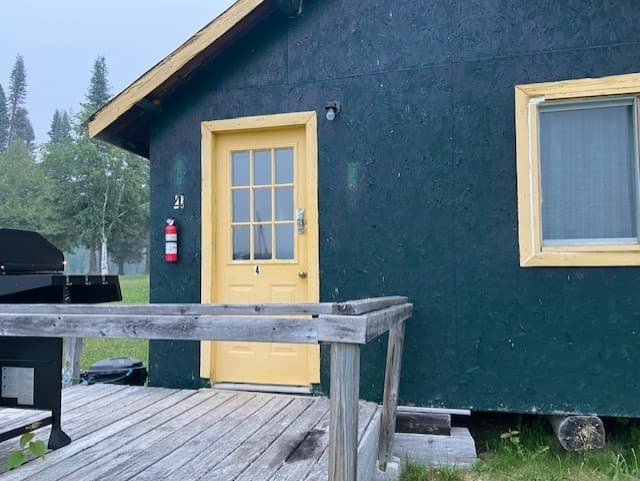 Yellow-door cabin entrance with small deck, lakeside outpost entry